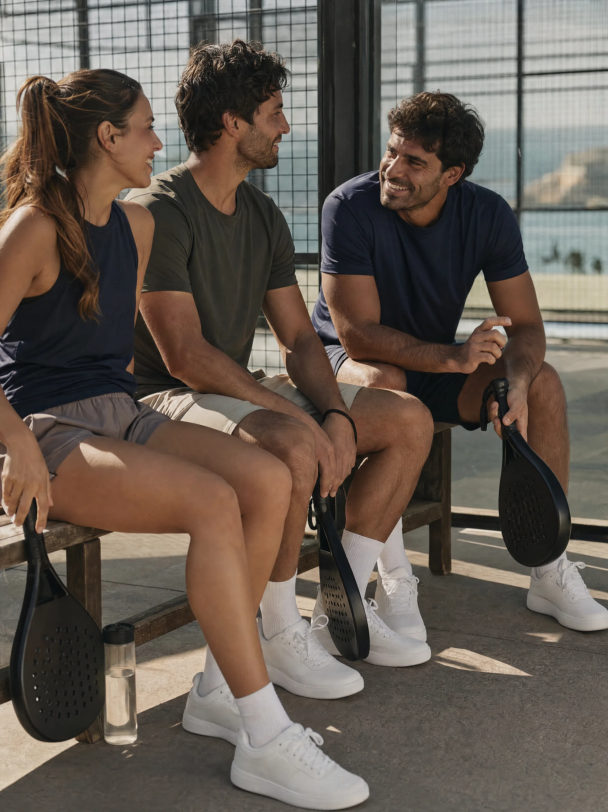 Three players talking on a bench at the court edge after a match